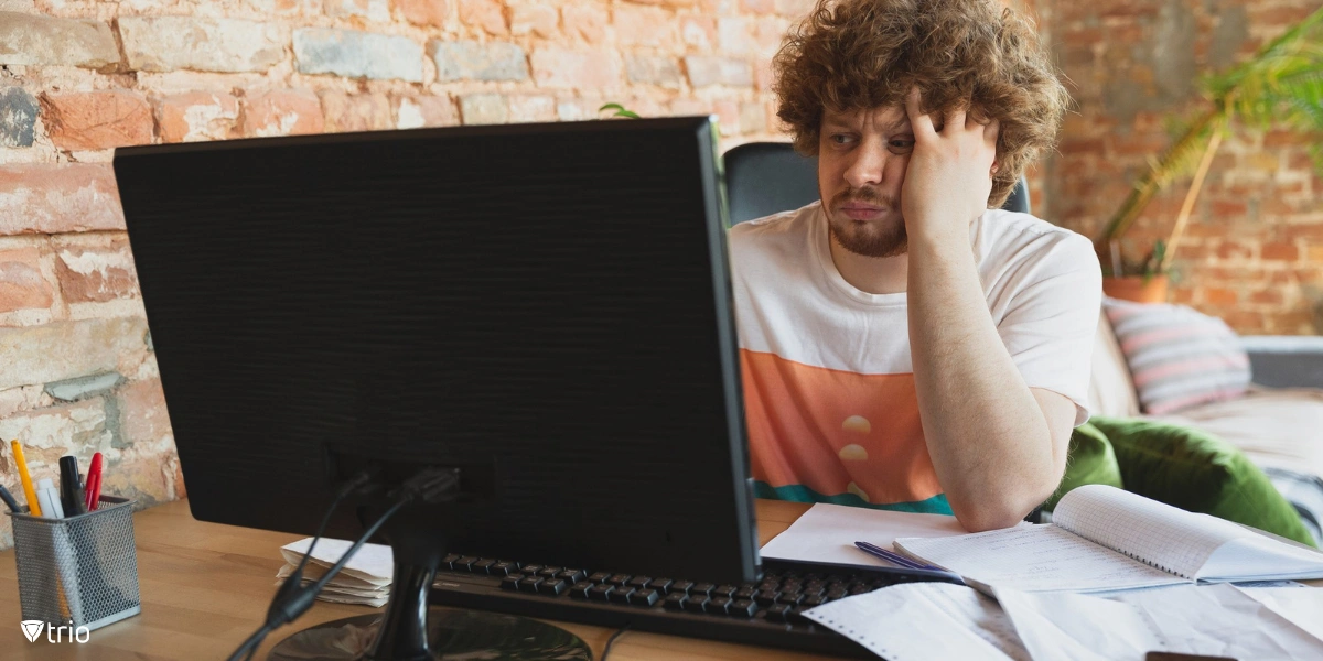 A frustrated man sitting at a desk with his head in his hands, looking at his laptop, appearing fed up with his slow PC.