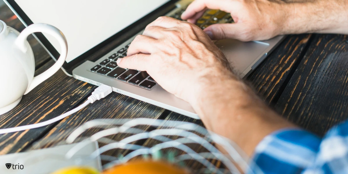 A close-up of a man's hand typing on a laptop at a wooden desk, testing software deployments on a few devices before organization-wide rollout to ensure a smooth, error-free implementation.