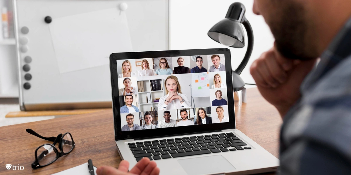 A person participates in a Zoom meeting, with a laptop screen displaying multiple participants in a virtual conference call.