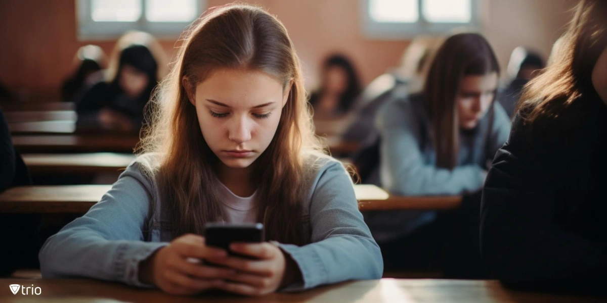 Girl in school looking at her phone sadly because she has seen derogatory posts about herself