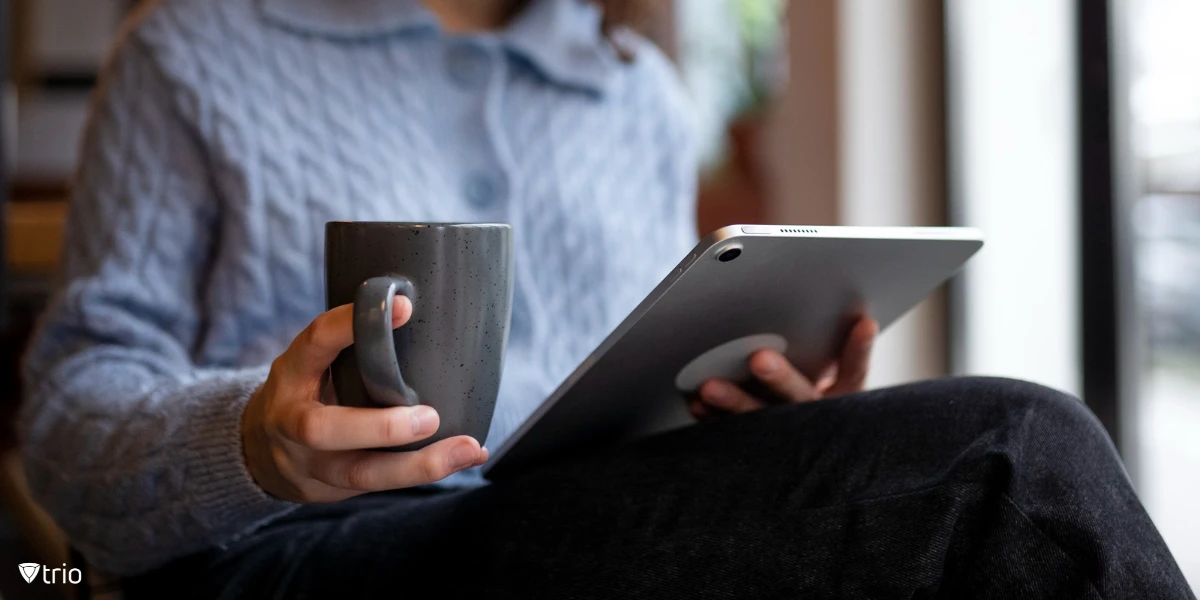 A person sits in a café, enjoying coffee while remotely accessing her Mac from her tablet.