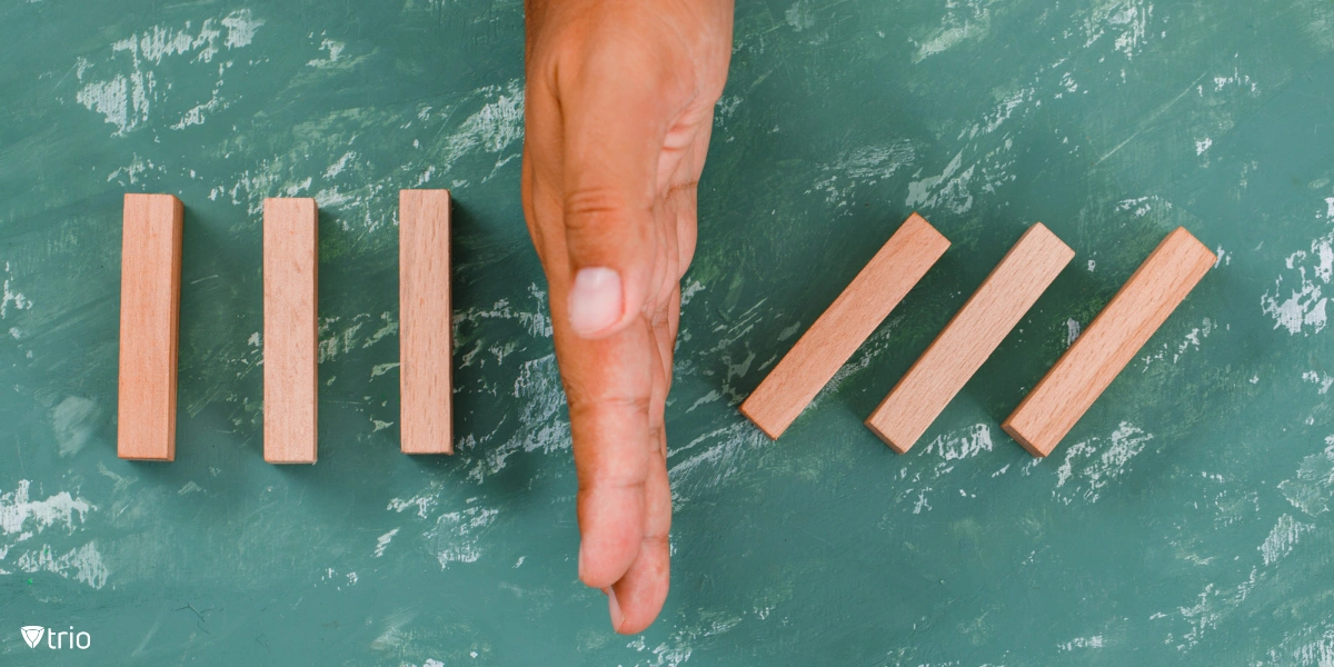 A hand acting as a barrier between falling wooden blocks, symbolizing the concept of minimizing risks.