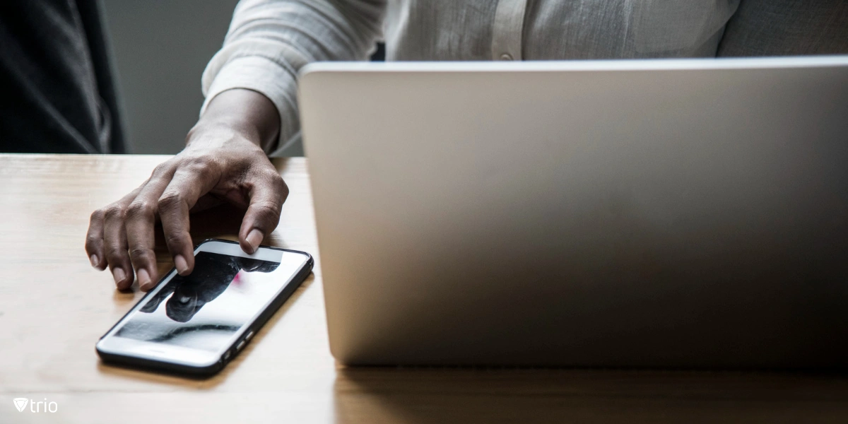 Eine Frau sitzt an einem Schreibtisch und arbeitet an einem Laptop in einem hellen Raum mit einem Mobiltelefon neben sich.