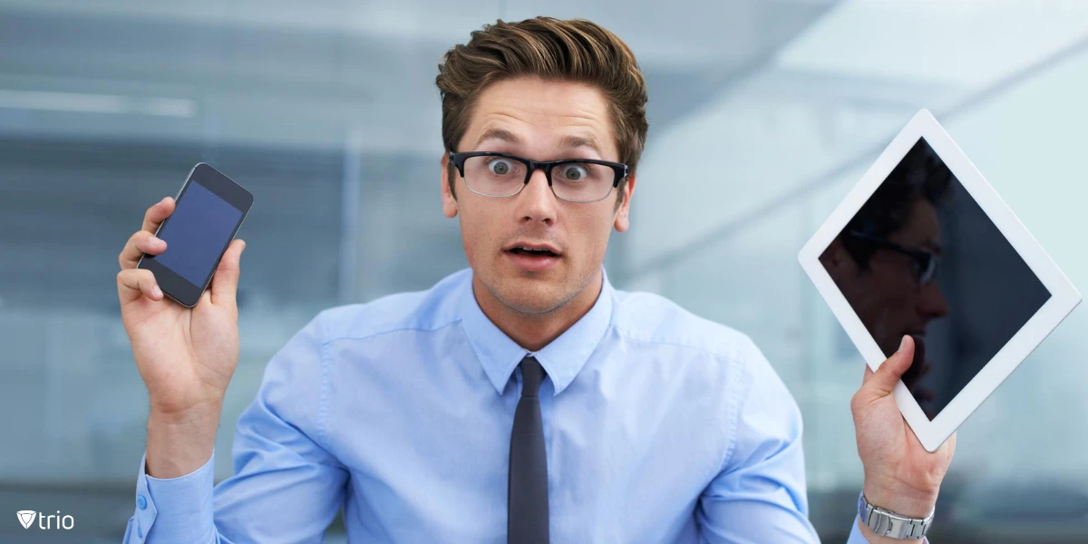 A business professional holding both a smartphone and tablet, looking confused and overwhelmed by choices.