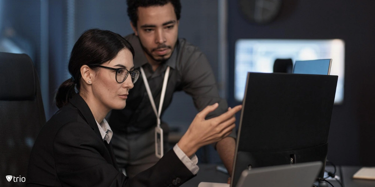 A senior project manager points to a computer screen while reviewing code, a security training session in a professional setting.