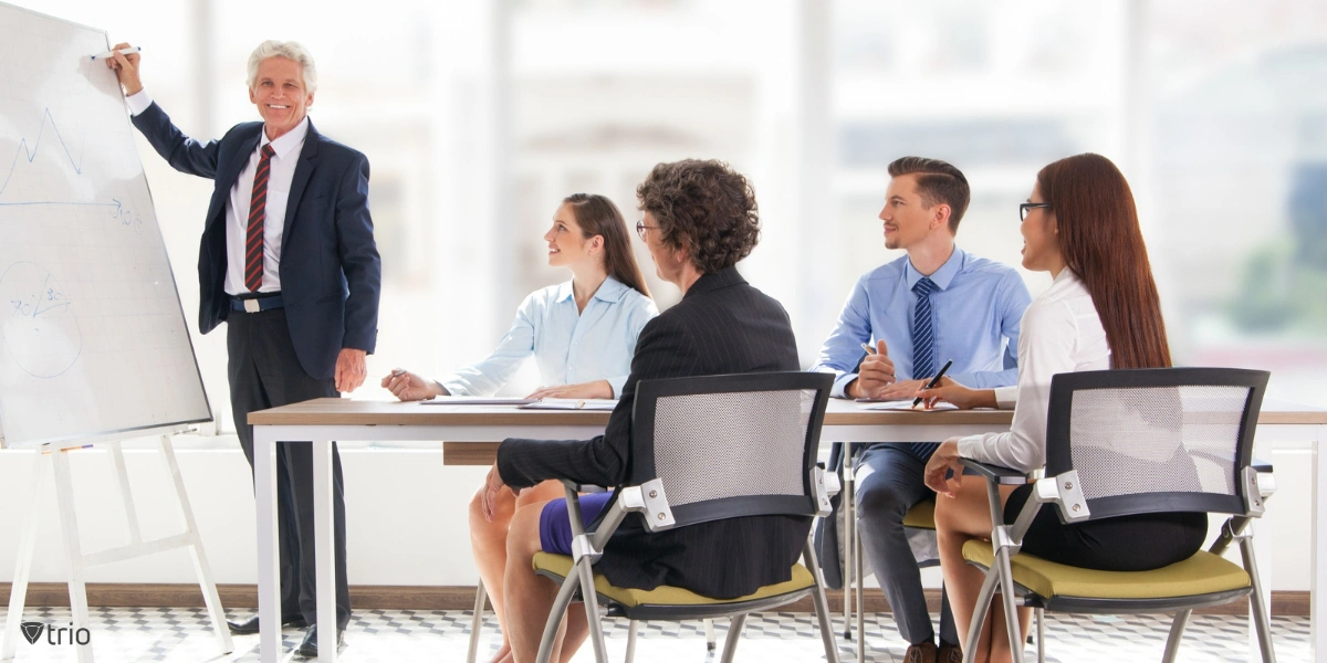 Group of mature business professionals participating in an employee training session in an office environment, with a speaker presenting and employees attentively listening and taking notes.