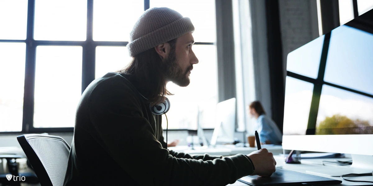 A man in an office sits at a desk using a computer, paying attention to track and evaluate system changes after they have been deployed.