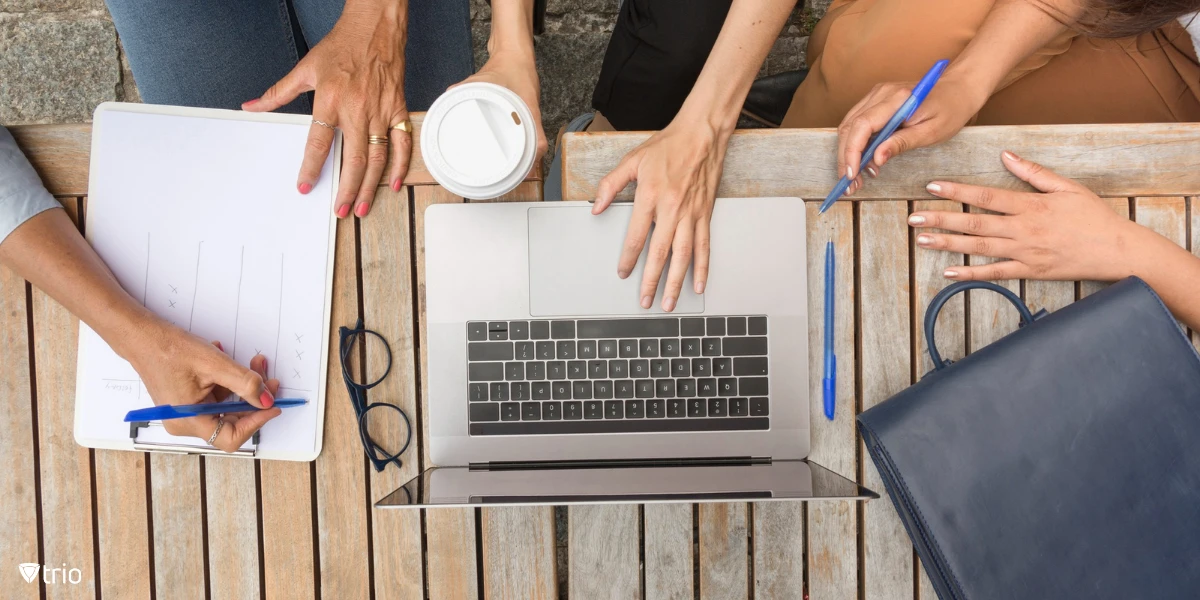 Top view of businesswomen working outdoors on laptops and documents, collaborating on data gathering and analysis in an open-air workspace.