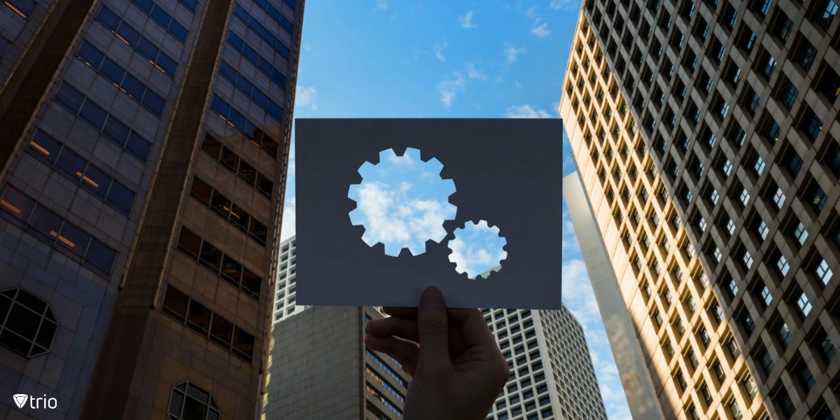 Interlocking gears on a perforated paper, set against a backdrop of tall buildings and sky.