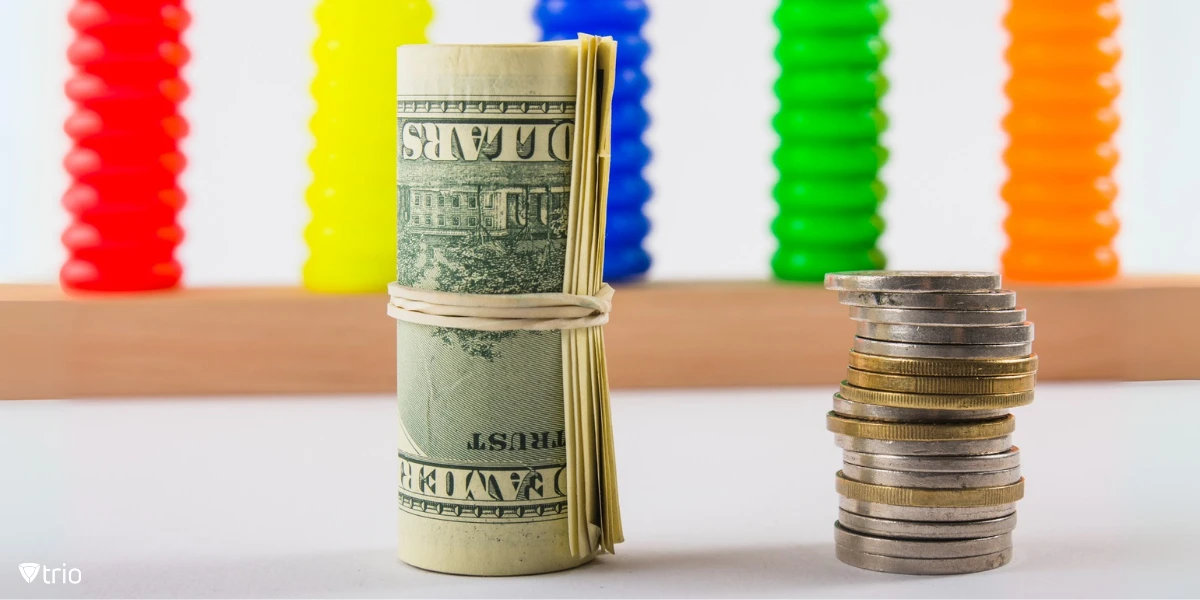 [A neat stack of coins is arranged on a table beside a rolled-up bundle of dollar bills tied with a rubber band.