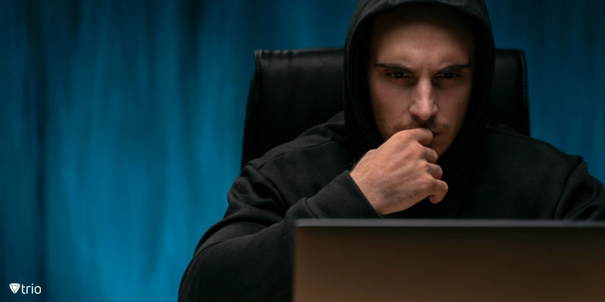 A suspicious guy in a black hoodie looking at a laptop monitor