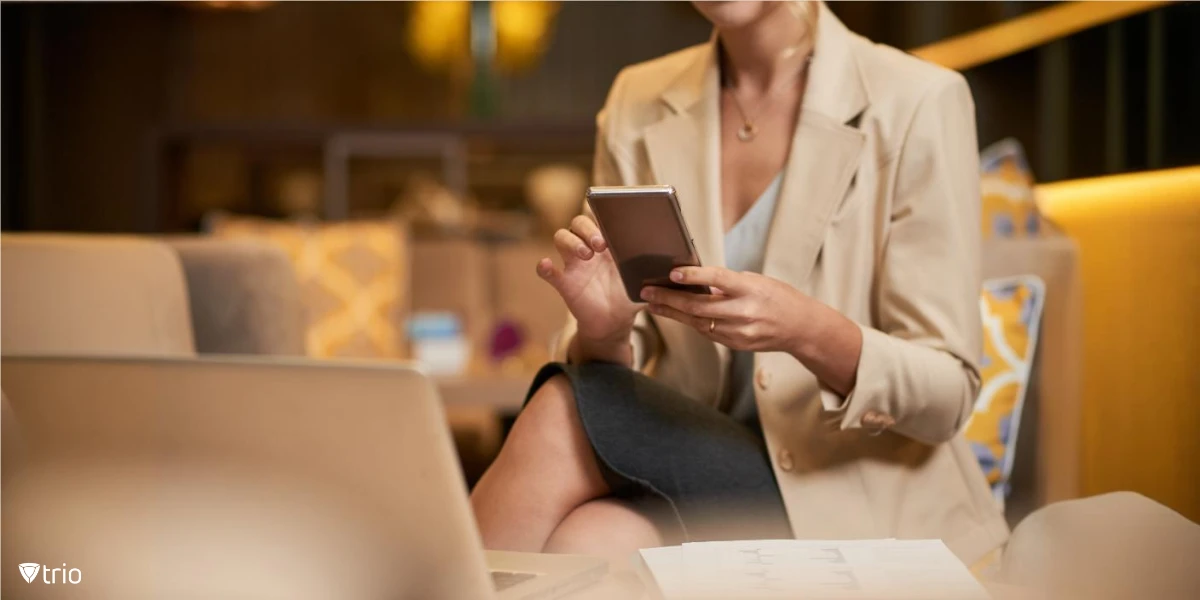 businesswoman using her phone while having a laptop on her desk