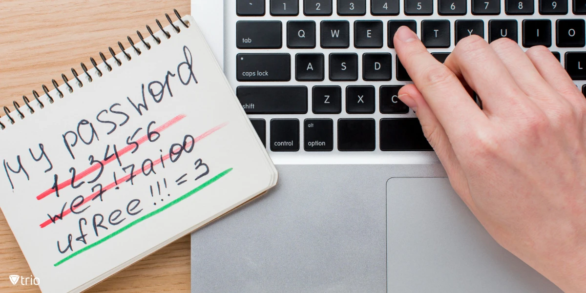 A person's hand typing on a laptop keyboard. Next to the laptop is a notebook with handwritten notes, including several crossed-out passwords.