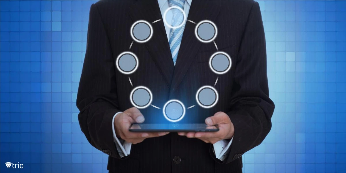 A man dressed in a dark business suit and striped tie is holding a tablet with a glowing interface. Above the tablet, there is a holographic circular diagram with empty nodes connected by dotted lines