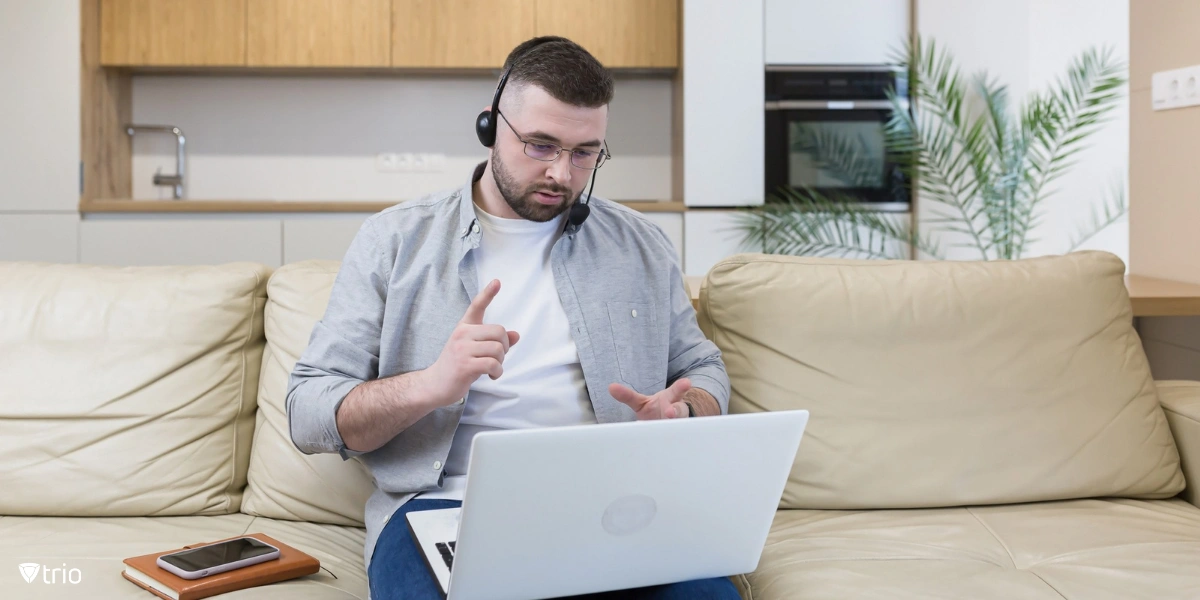 Man working from home sitting on the couch & using a laptop and a headset with a microphone]