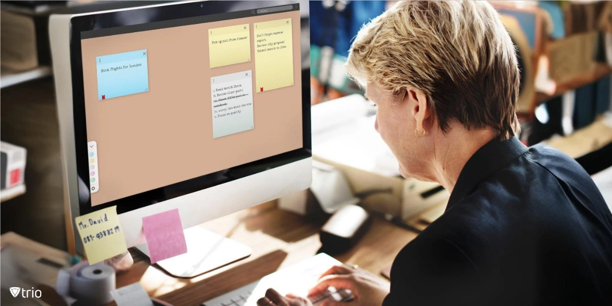 A person is sitting at a computer, looking at digital sticky notes displayed on a large monitor