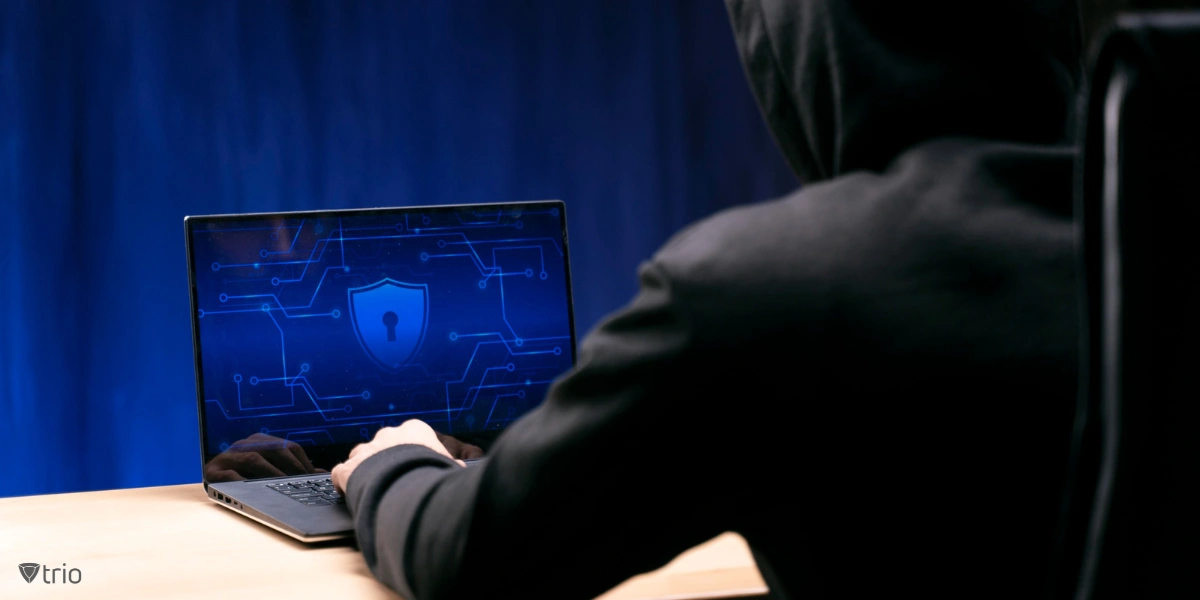 man with hoodie sitting in front of laptop with shield and lock on the screen