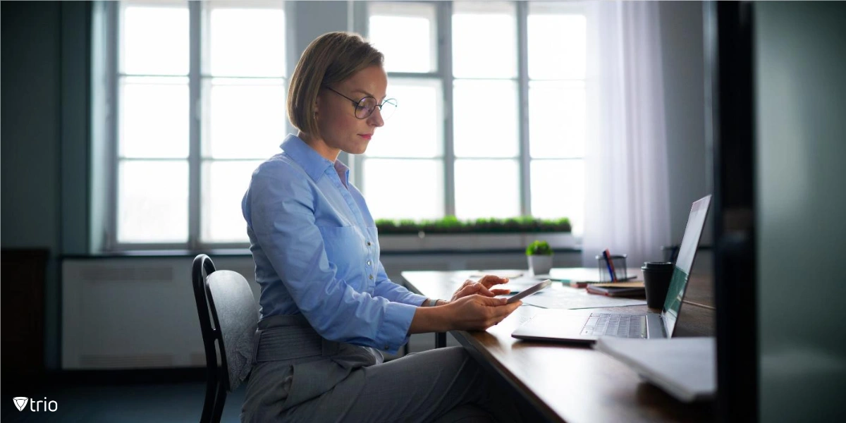 Businesswoman using her phone while sitting at a desk in front of her laptop