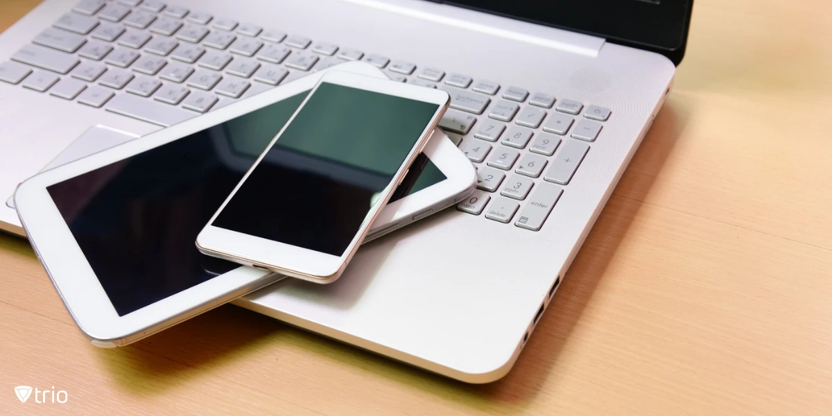 A silver laptop with a tablet and smartphone placed on top.