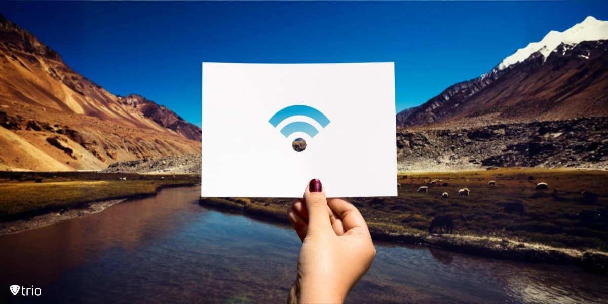 A hand holds a piece of perforated paper with a Wi-Fi symbol cut out, set against a stunning natural landscape with mountains and a river.